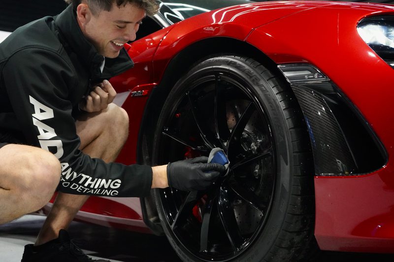 Detailing the wheels of a red supercar in branded uniform