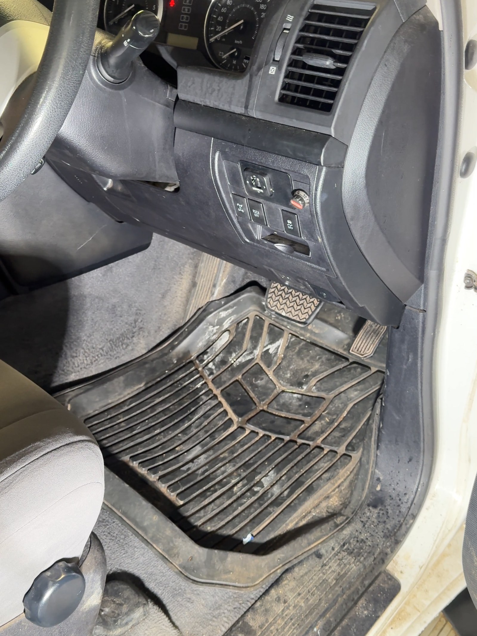 The driver footwell of a work vehicle before cleaning, the rubber mat packed with dried mud