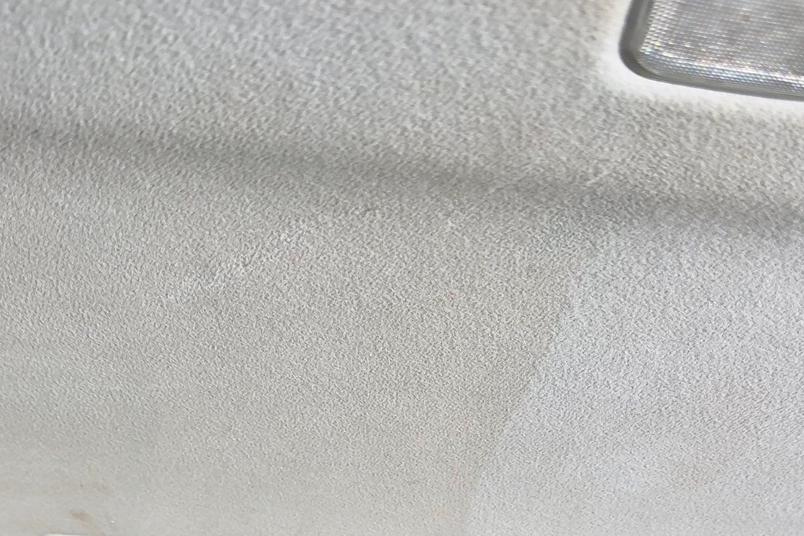 A roof lining photographed part way through cleaning, the untouched left half still grey against the finished right half